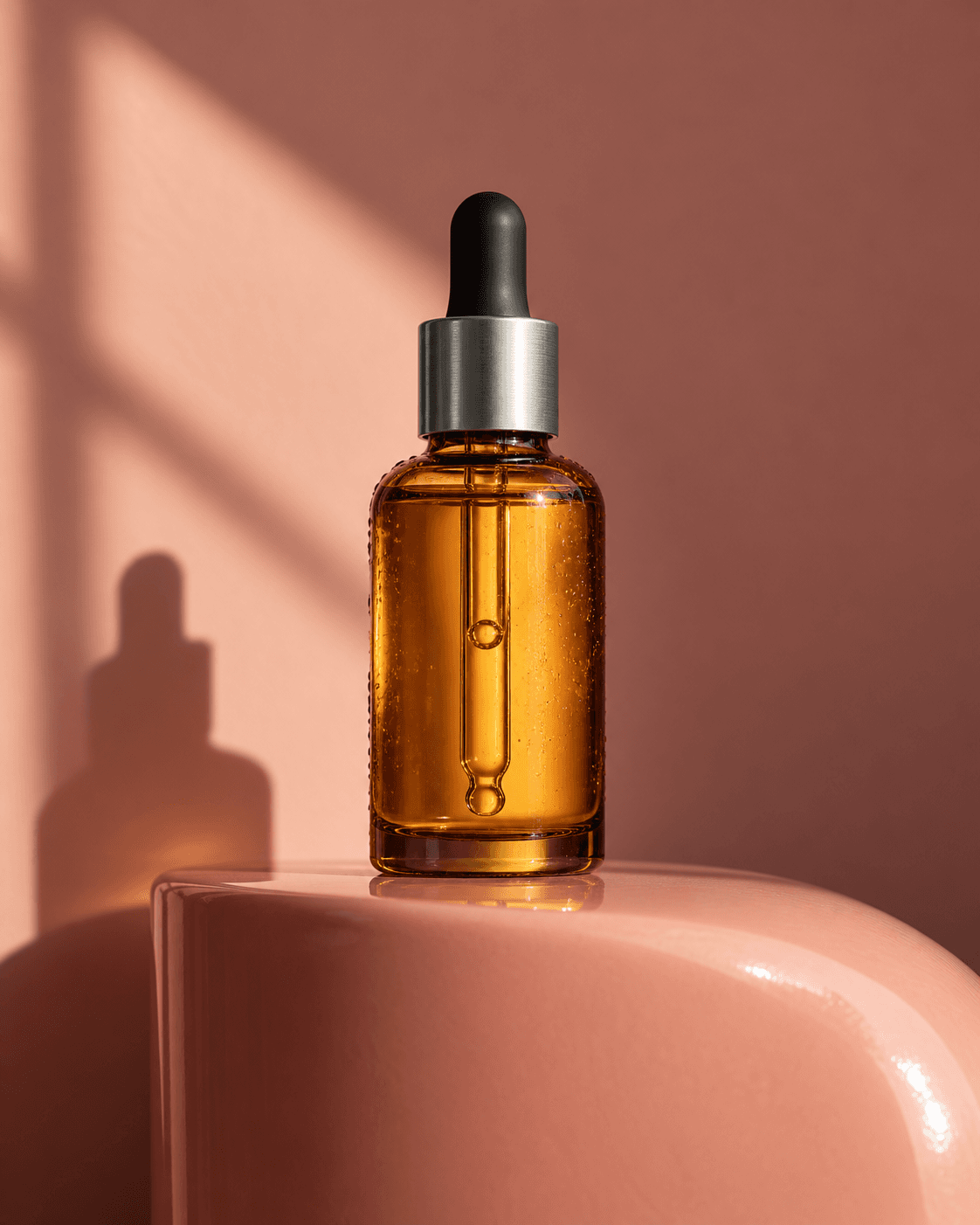 Original concept still: an amber serum bottle on a coral plinth in warm directional light